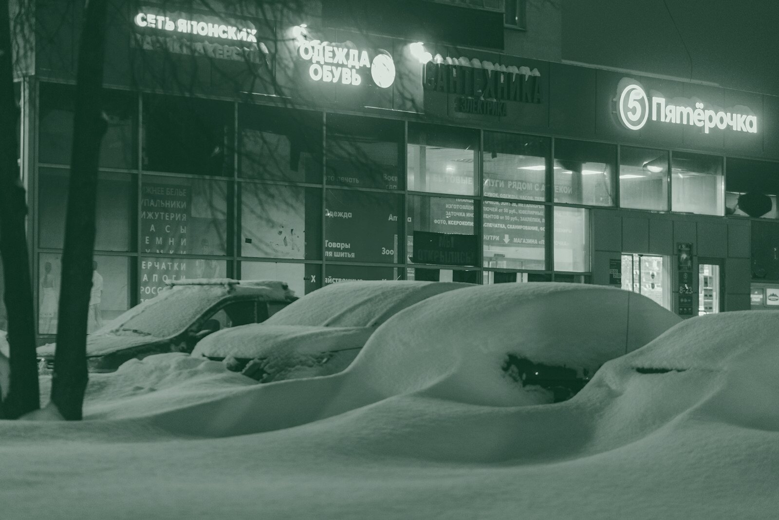 Cars parked in snow outside a brightly lit store